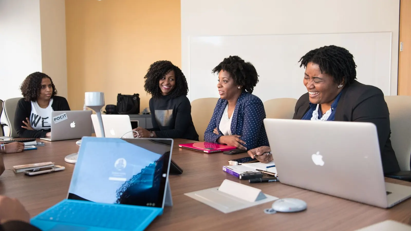 A group discussing work around an office table with laptops and notebooks.