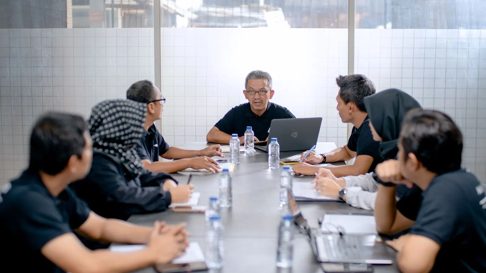 A group discussing work around a long conference table with open laptops.