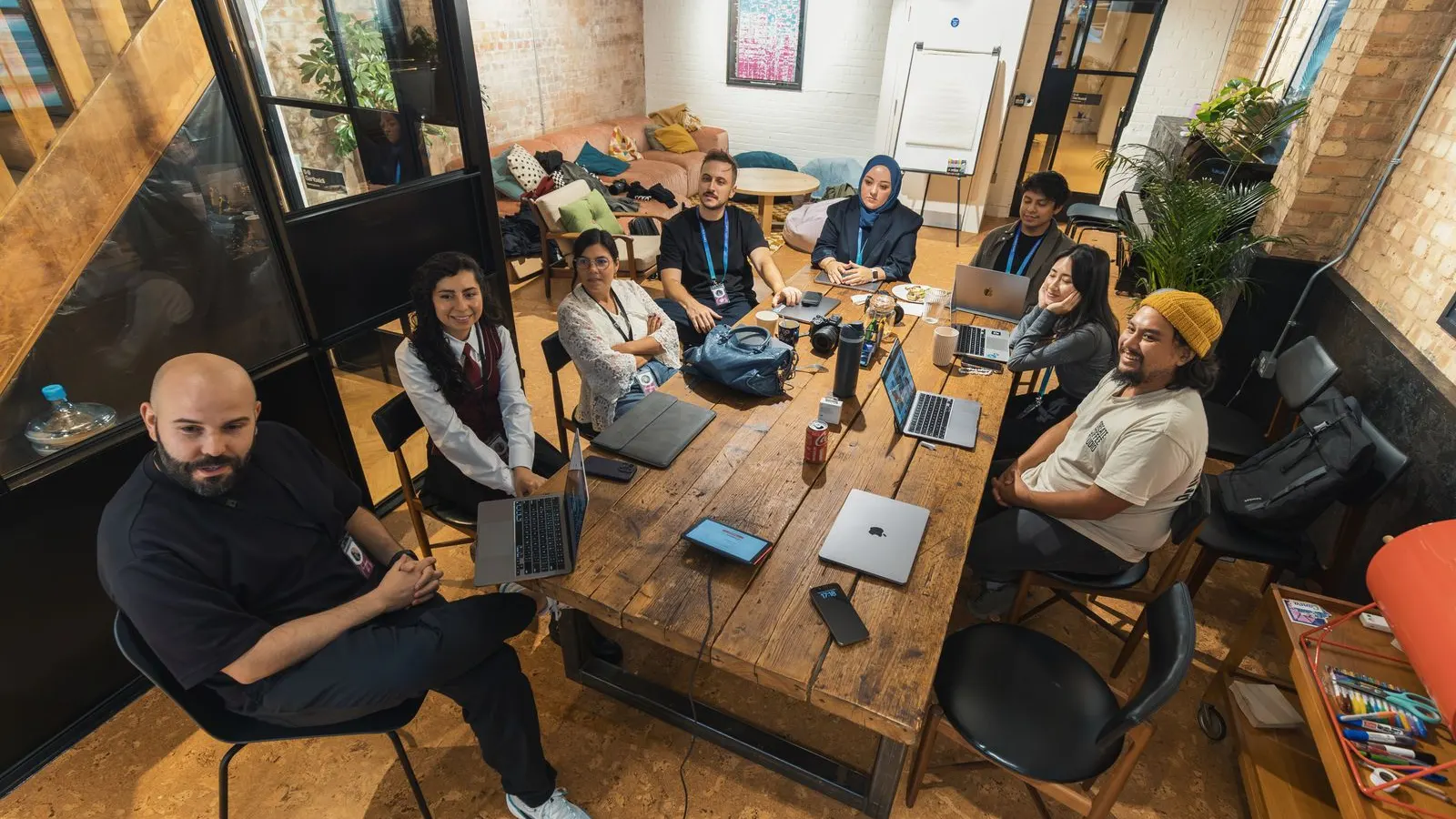 A large group collaborating with laptops around a long wooden table.