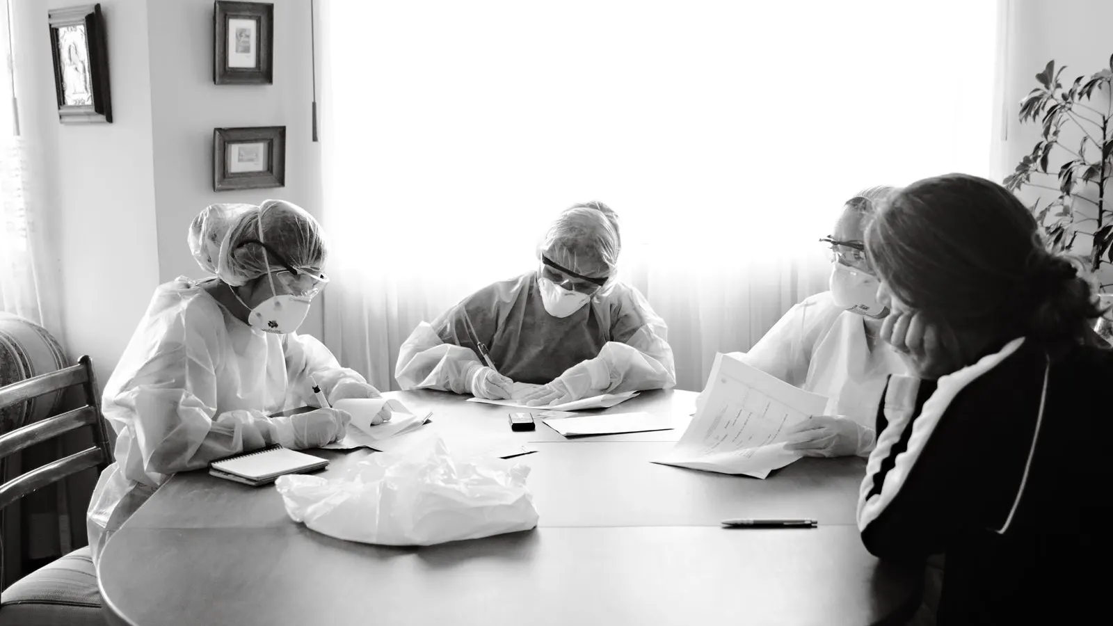 Healthcare workers in protective clothing discussing documents around a table.