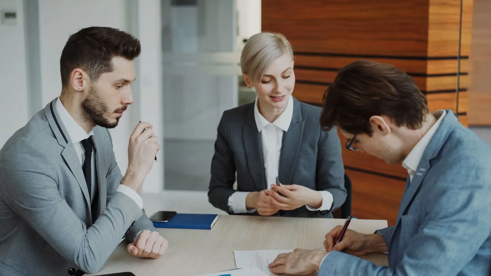 Three colleagues discussing documents and a laptop around an office table.