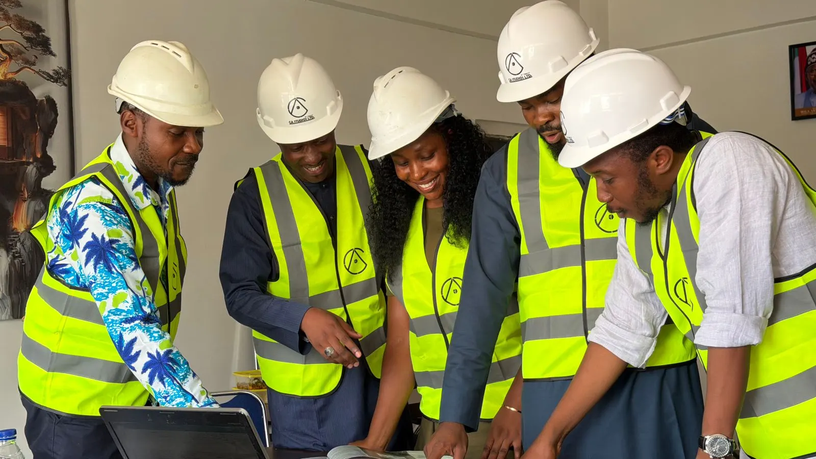 A group wearing hard hats and safety vests reviewing plans together indoors.