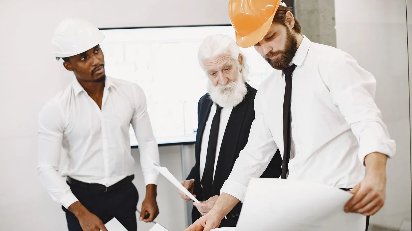 Colleagues in hard hats reviewing a large plan together at an office desk.