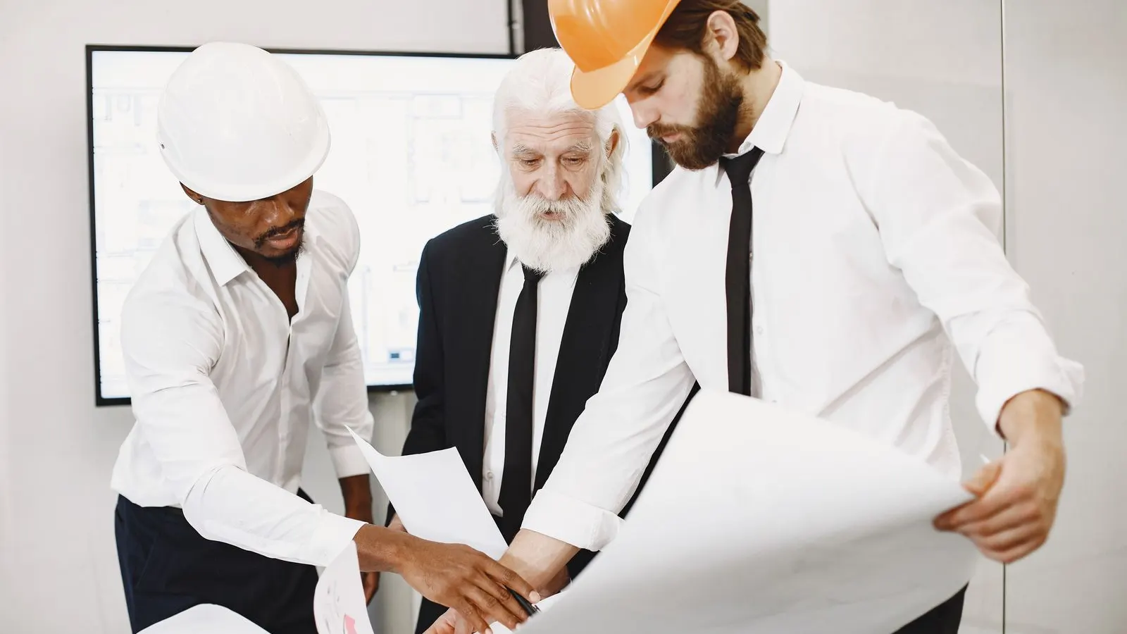 Three colleagues in hard hats discussing a large plan together in an office.