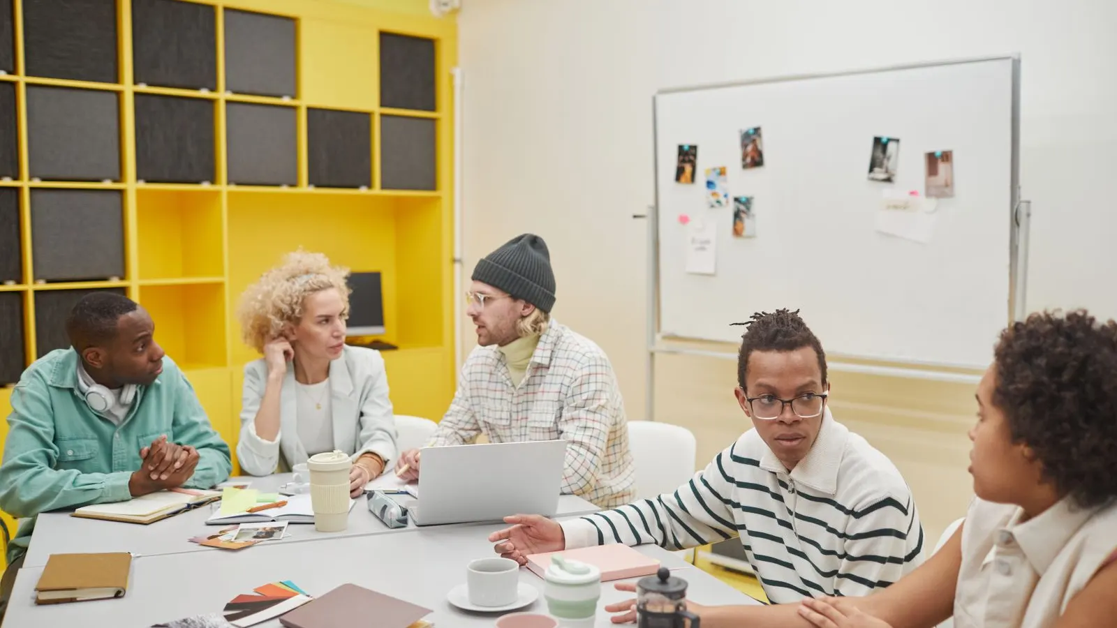 Colleagues exchanging ideas around a white table in a colorful workspace.