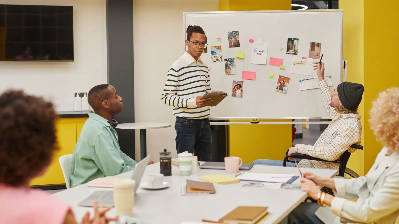 A colleague presenting sticky notes on a whiteboard to a seated team.