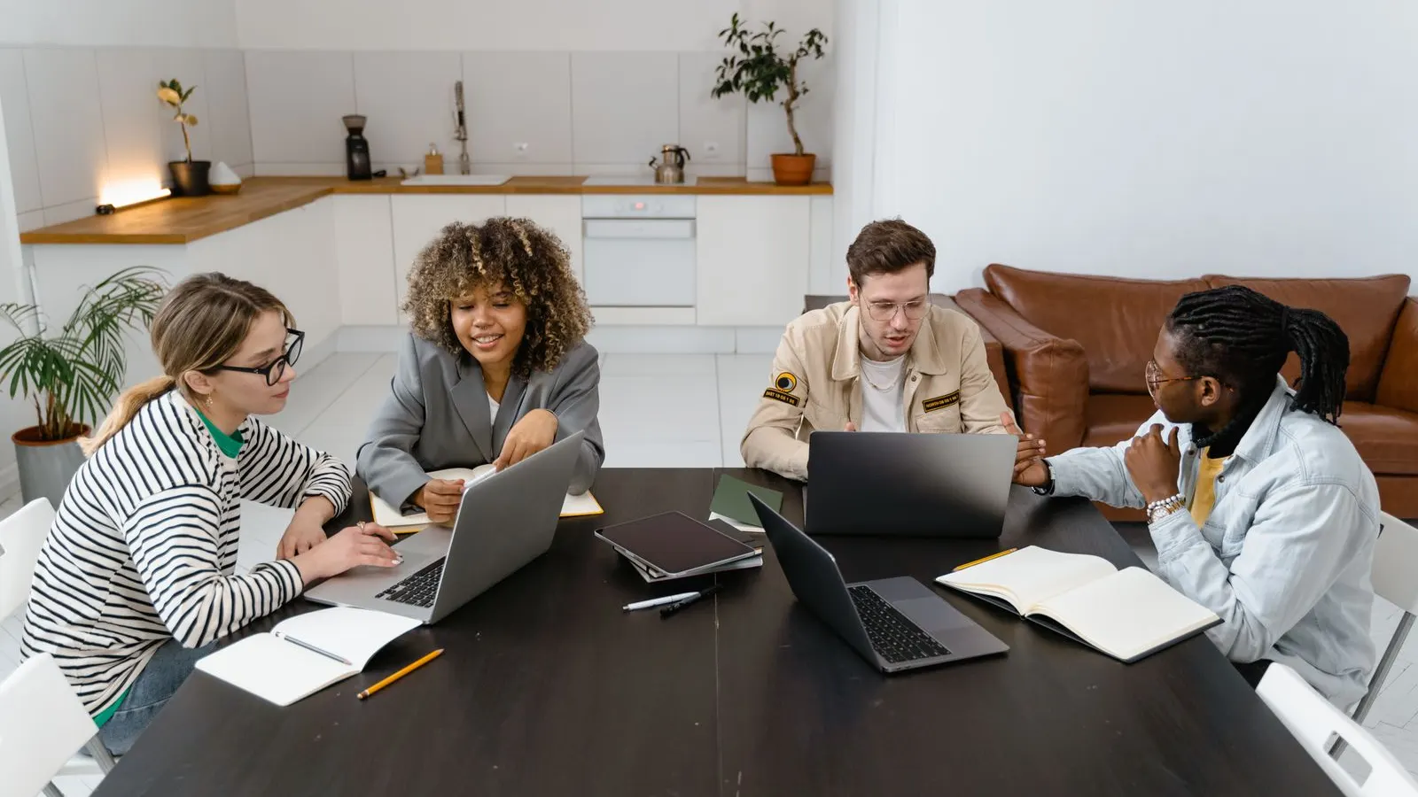 A team discussing laptops and documents around a long table in a bright office.