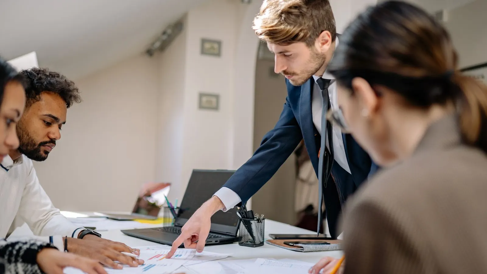 A colleague points to printed diagrams as teammates review the work around a table.