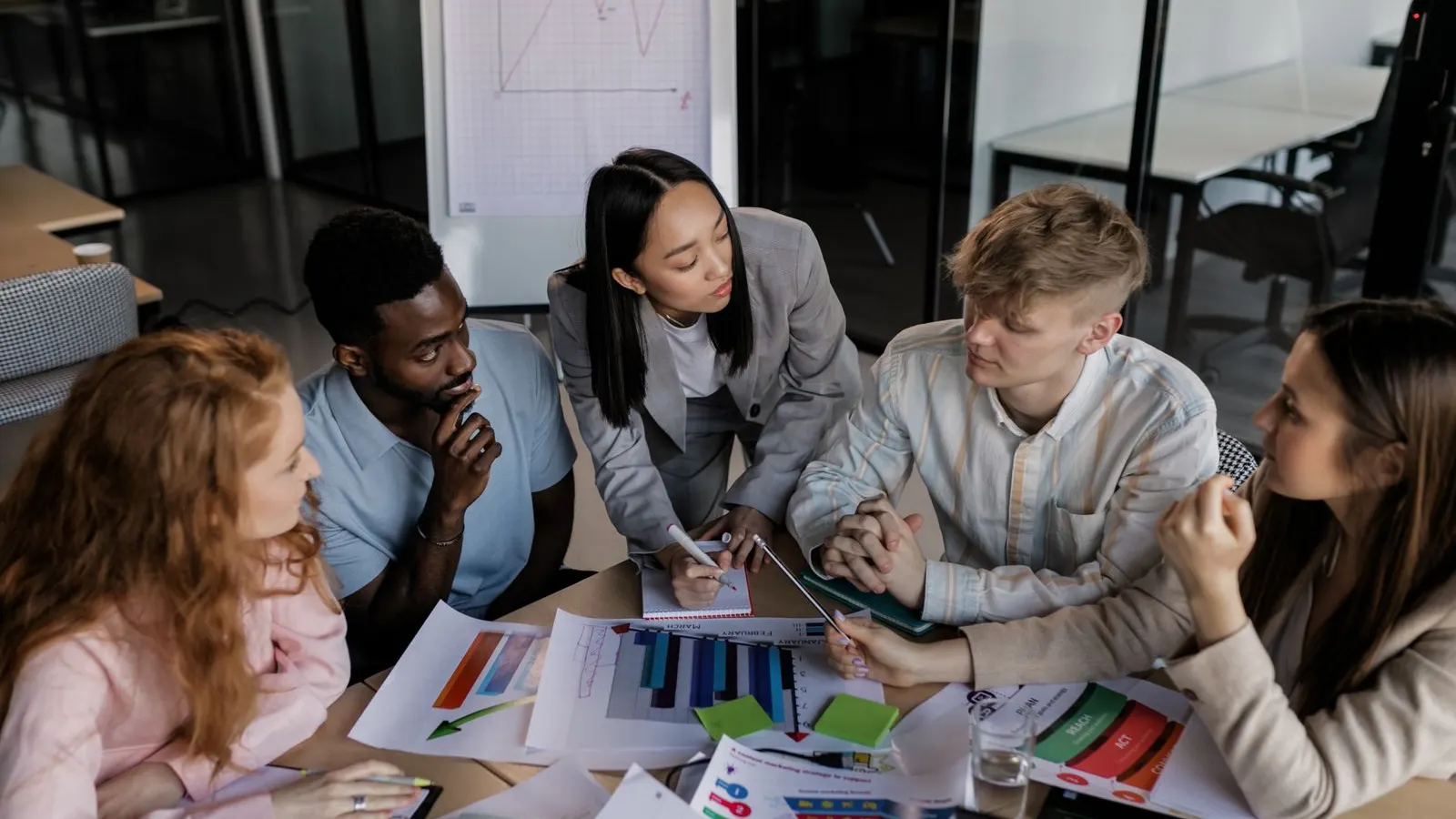 A group leaning over printed charts and laptops during a shared working session.