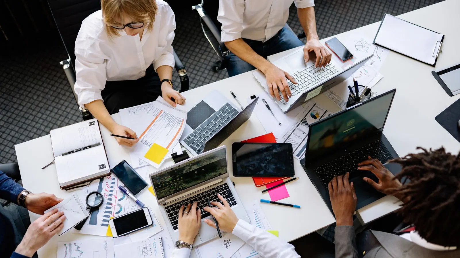 An overhead view of colleagues reviewing plans, notes and laptops around a worktable.