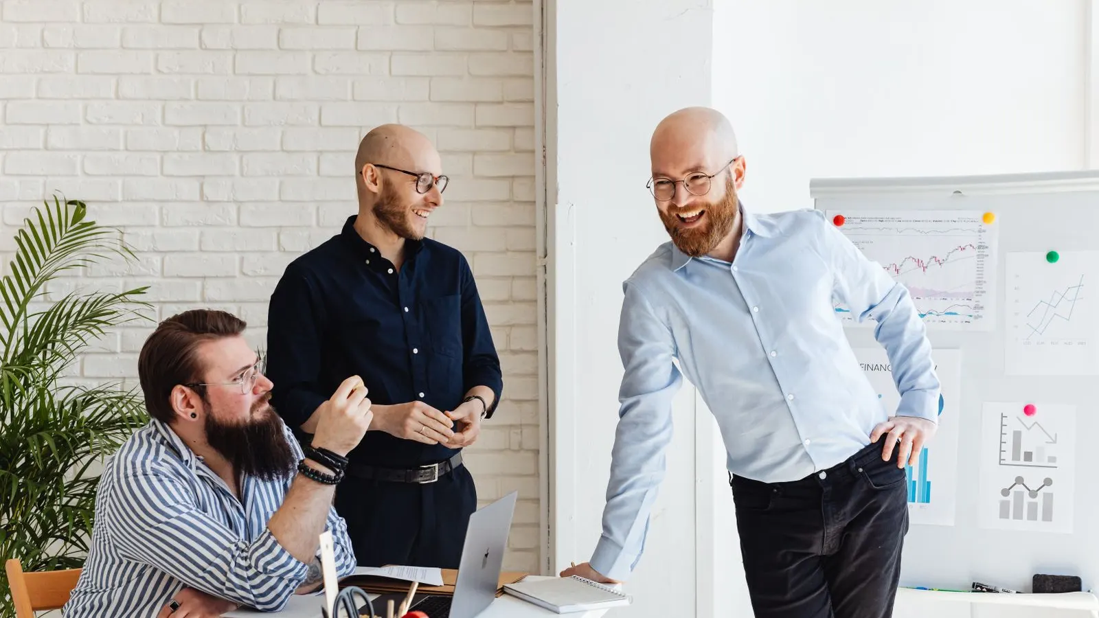 Three colleagues discussing ideas beside a whiteboard in a bright workspace.