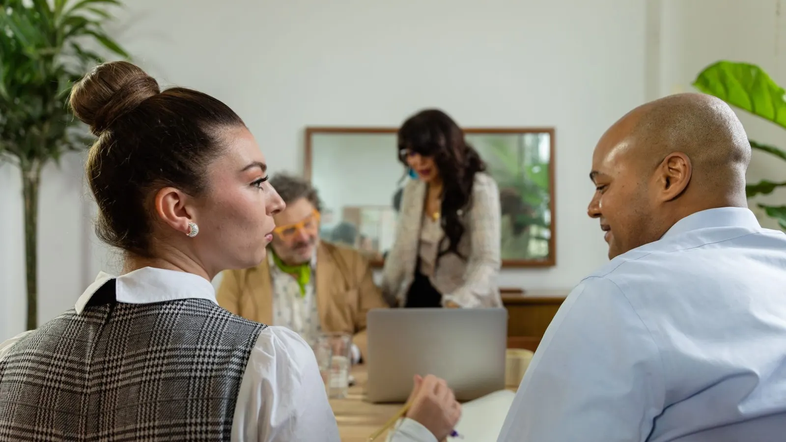 Two colleagues discuss their work across a laptop during an office team meeting.