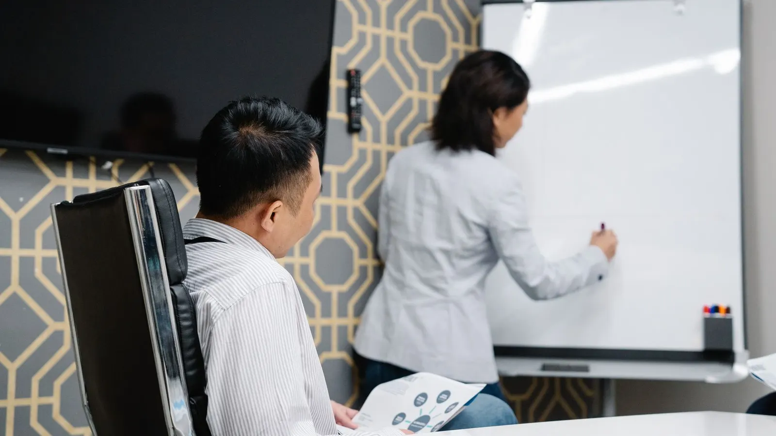 Colleagues following a whiteboard explanation with laptops and notes nearby.