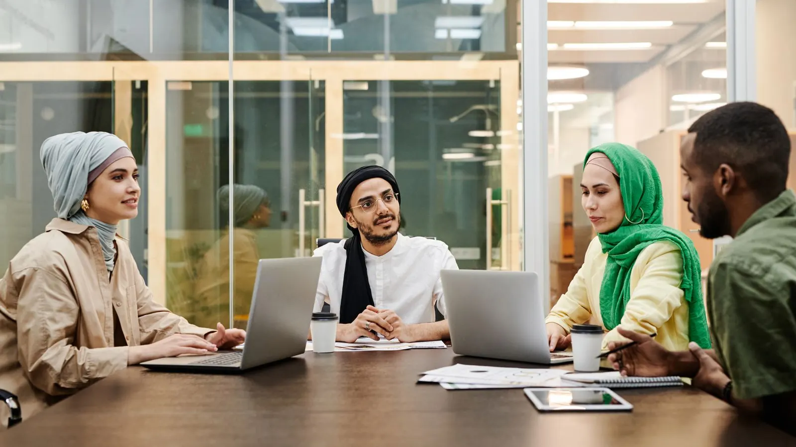 Four colleagues discussing ideas with laptops and a tablet at a shared table.