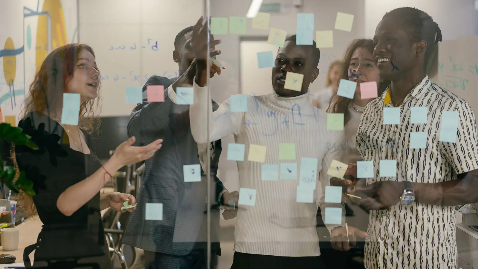 A team arranging sticky notes together on a glass planning wall.